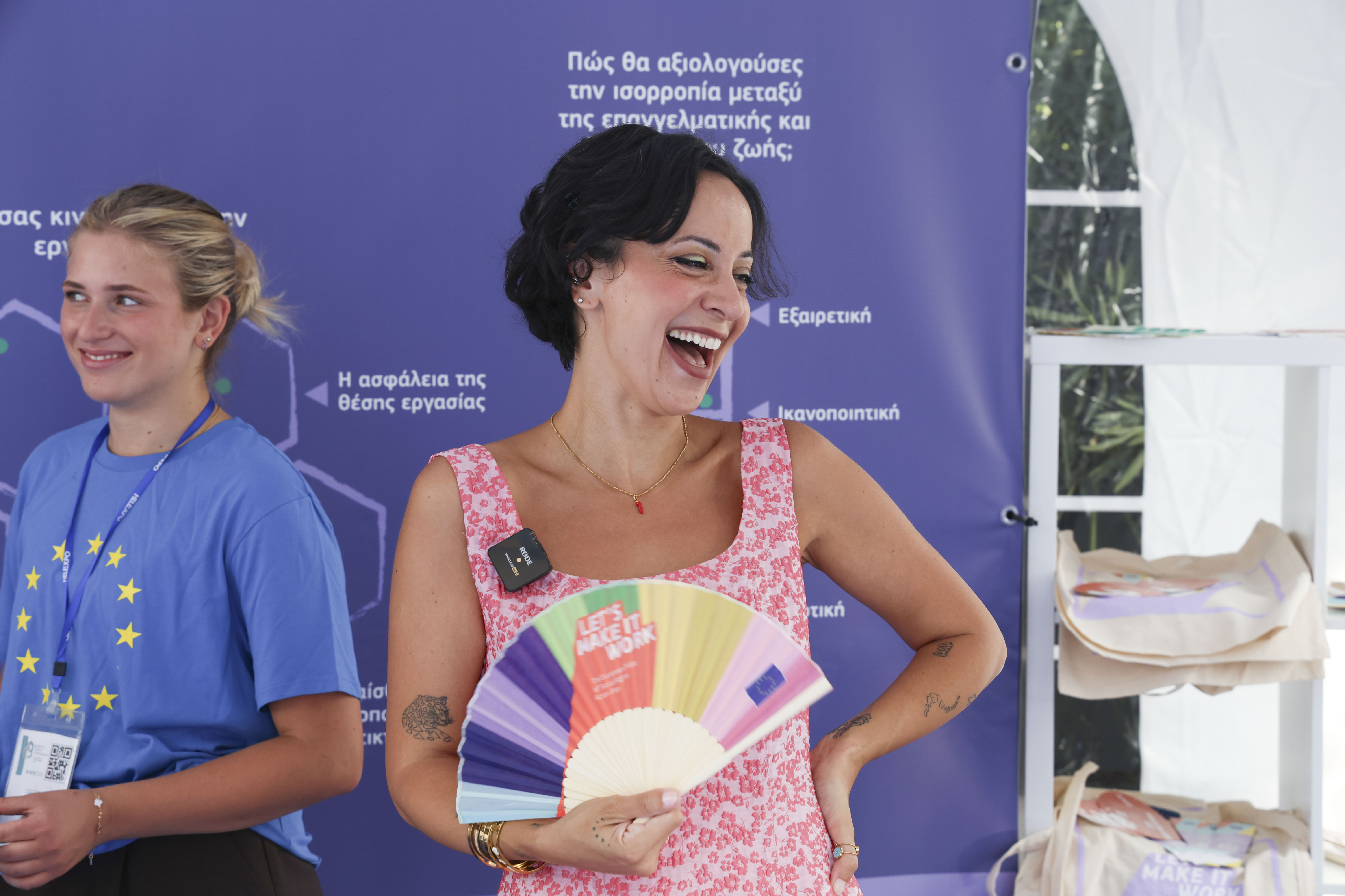 Iné laughing at an event stand, holding a fan